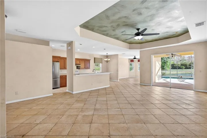 Unfurnished living room featuring a chandelier, healthy amount of natural light, a ceiling fan, and a raised ceiling
