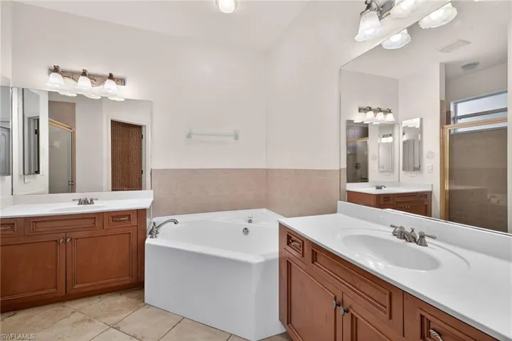 Full bathroom with a shower stall, two vanities, a bath, and light tile patterned flooring