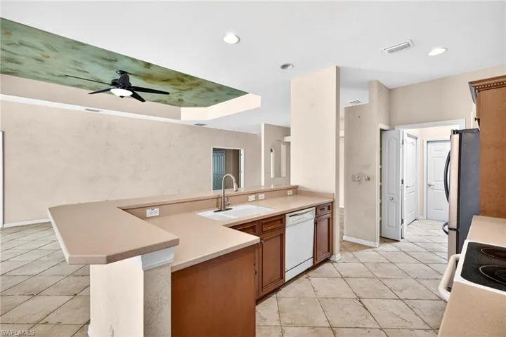 Kitchen featuring wood finish cabinets, white appliances, a ceiling fan, a peninsula, and a tray ceiling