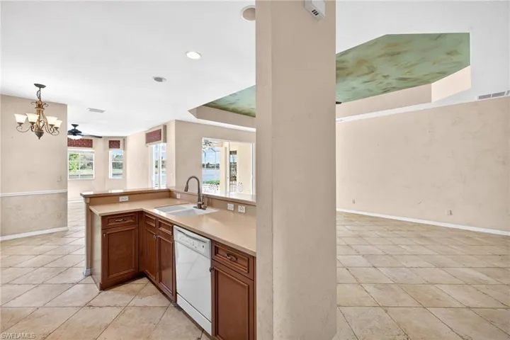 Kitchen featuring light countertops, suspended lighting, white dishwasher, wood finish cabinets, and open floor plan