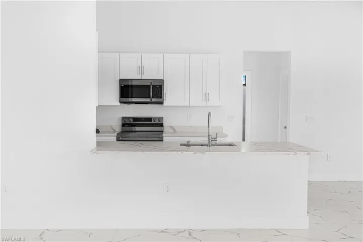 Kitchen featuring a sink, stainless steel appliances, marble finish floor, and white cabinetry