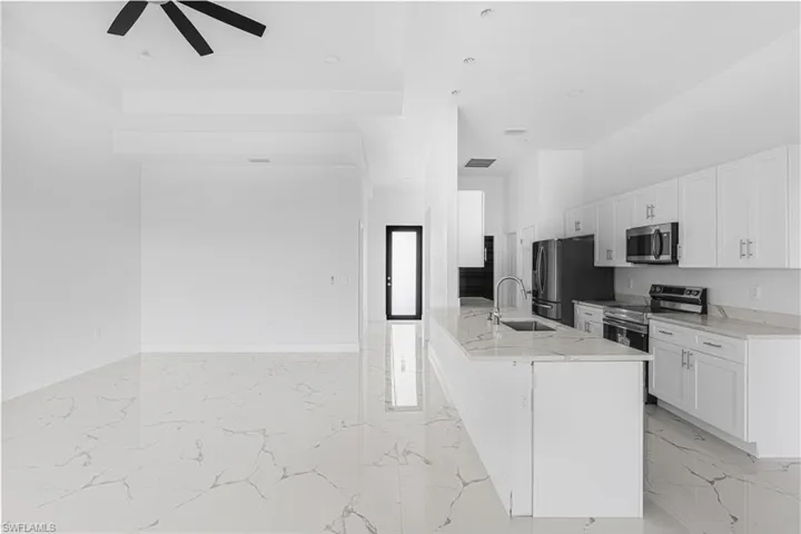 Kitchen with marble finish floor, a ceiling fan, a sink, white cabinetry, and appliances with stainless steel finishes