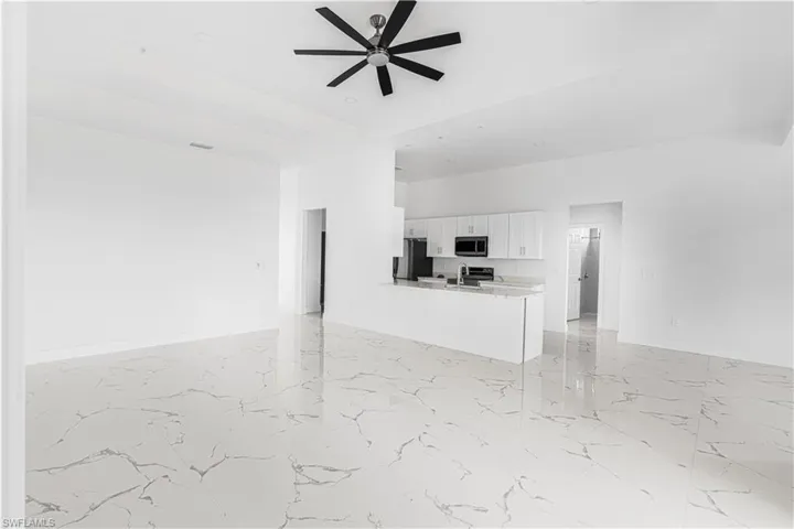 Kitchen featuring stainless steel microwave, ceiling fan, freestanding refrigerator, white cabinets, and marble finish floor
