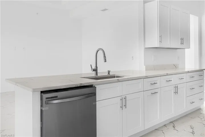Kitchen with a sink, light stone counters, stainless steel dishwasher, and marble finish floor