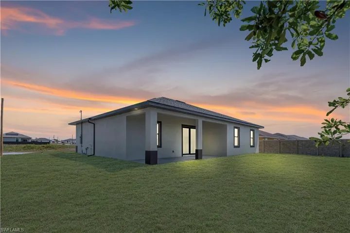 Back of house at dusk featuring stucco siding, a lawn, and fence