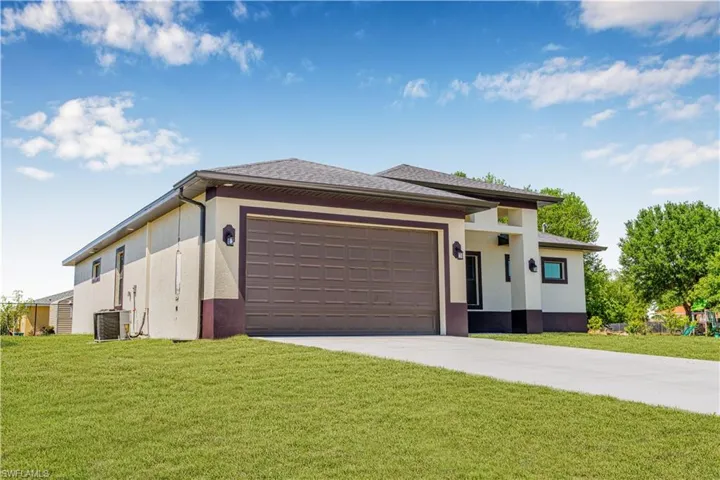 Prairie-style home featuring stucco siding, driveway, a front lawn, an attached garage, and central AC unit