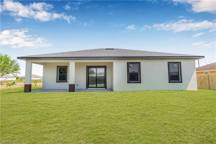 Rear view of property with a lawn, a shingled roof, fence, and stucco siding