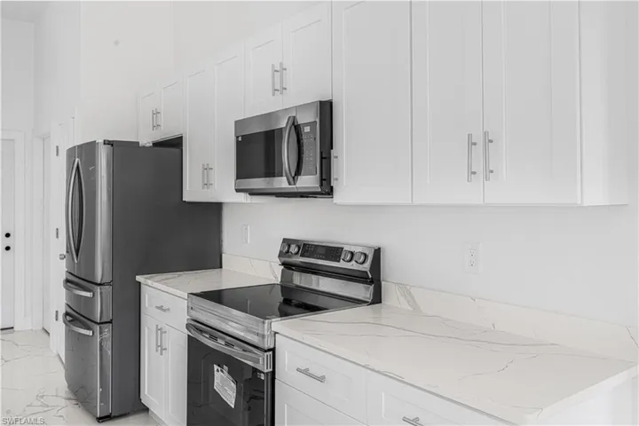 Kitchen with light stone countertops, marble finish floor, appliances with stainless steel finishes, and white cabinets