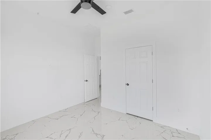 Empty room featuring a ceiling fan, visible vents, marble finish floor, and baseboards