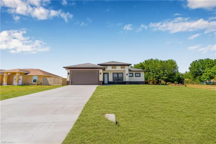 Prairie-style home with a garage, stucco siding, driveway, and a front lawn