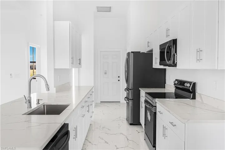 Kitchen with light stone counters, visible vents, a sink, black appliances, and marble finish floor