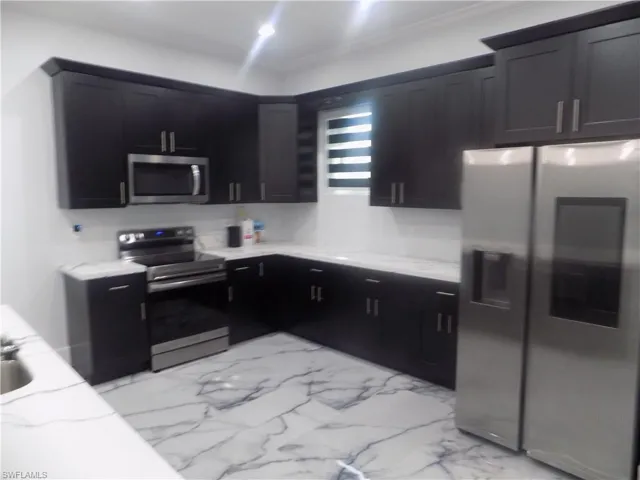 Kitchen with appliances with stainless steel finishes, dark cabinetry, light stone counters, crown molding, and light marble finish floors