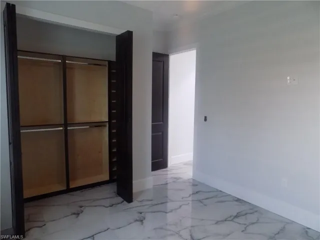 Unfurnished bedroom featuring marble finish flooring, a closet, and ornamental molding