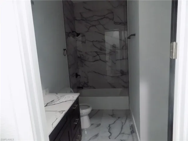 Bathroom featuring marble look tiles, vanity, and a marble finish shower