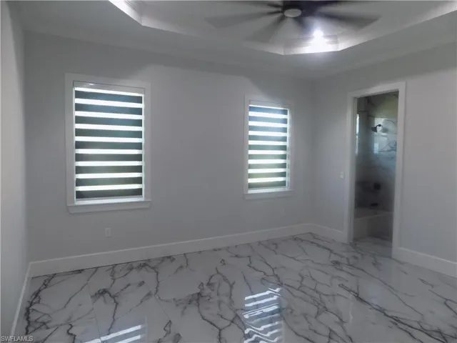 Spare room with a raised ceiling, a ceiling fan, marble look tiles, and crown molding