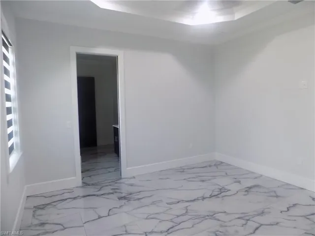 Spare room featuring marble finish floors, a raised ceiling, plenty of natural light, and ornamental molding