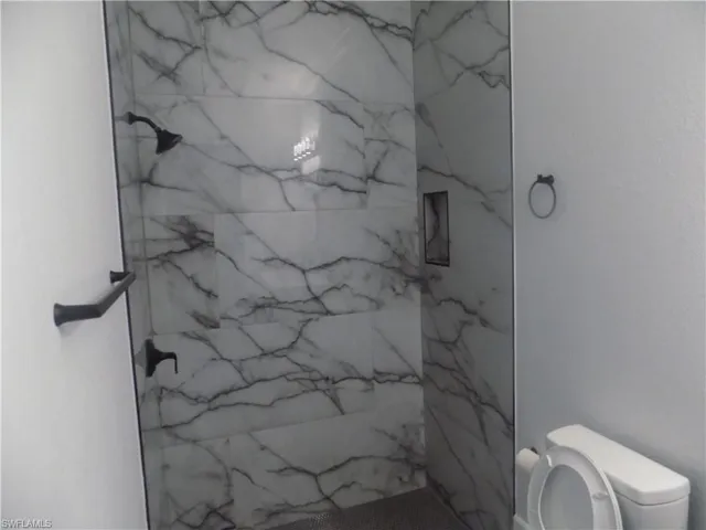 Bathroom featuring toilet and a marble finish shower