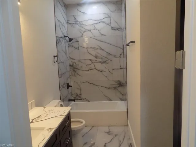 Full bathroom with marble look tiles, vanity, and shower / bathtub combination