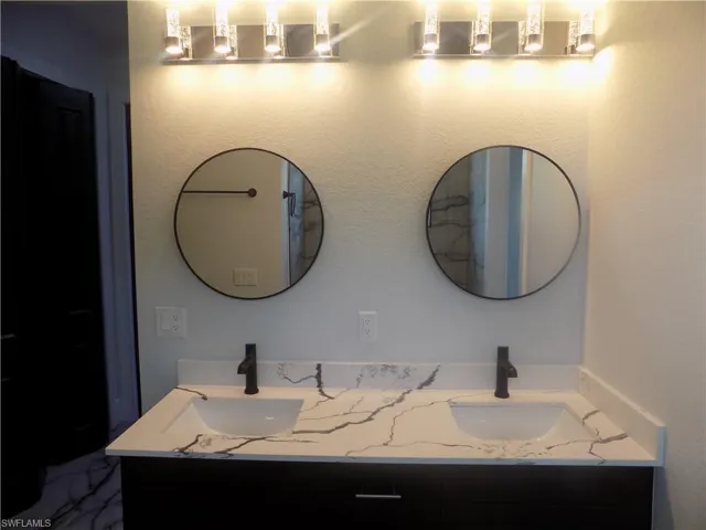 Full bath featuring double vanity and marble finish floors