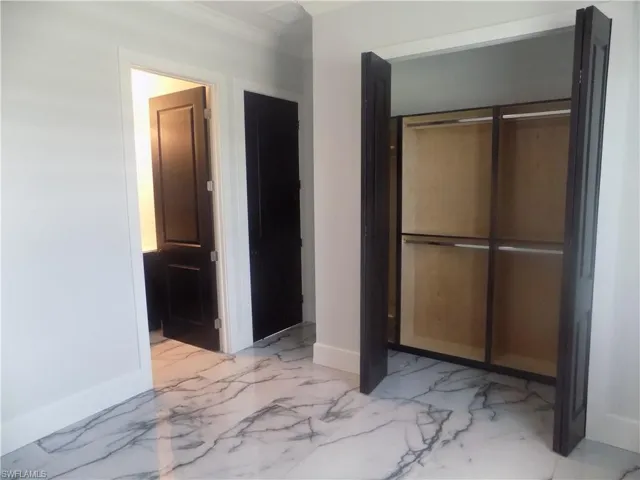 Unfurnished bedroom with light marble finish floors, a closet, and crown molding