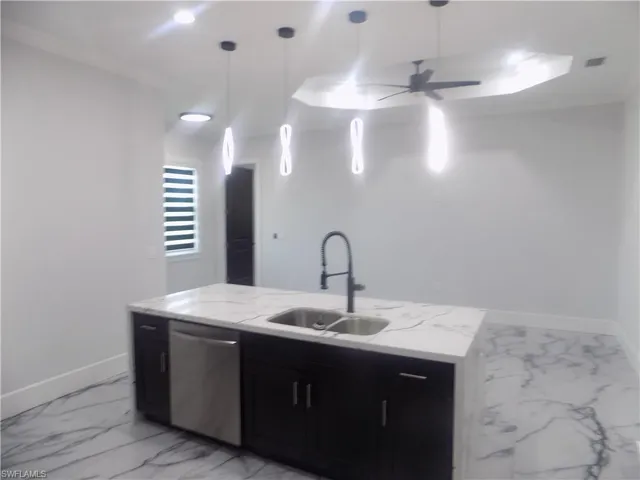 Kitchen featuring stainless steel dishwasher, light marble finish floors, dark cabinets, a ceiling fan, and light stone countertops