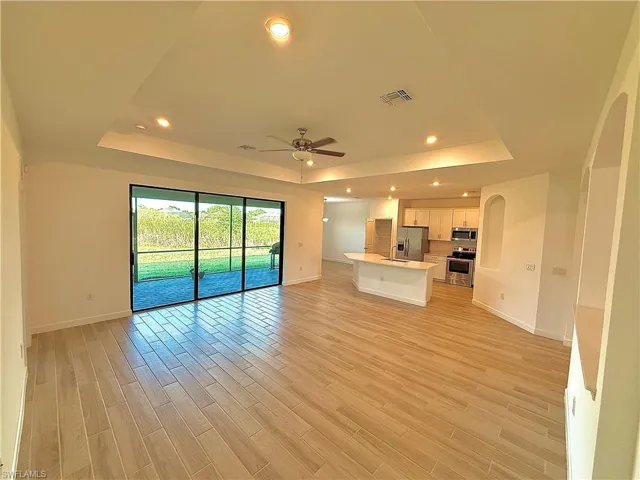 Unfurnished living room with a raised ceiling, ceiling fan, recessed lighting, light wood-style floors, and arched walkways