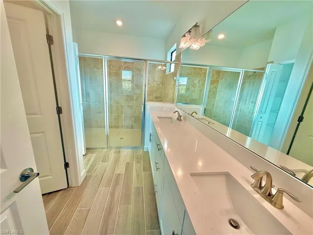 Bathroom with a stall shower, double vanity, wood tiled floors, and recessed lighting