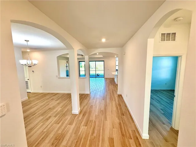 Corridor featuring arched walkways, light wood finished floors, and a chandelier