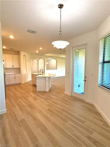Kitchen with decorative light fixtures, light wood-type flooring, white cabinets, and an island with sink