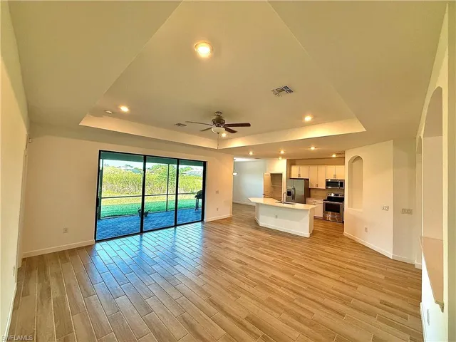 Unfurnished living room featuring a tray ceiling, recessed lighting, a ceiling fan, and light wood-type flooring