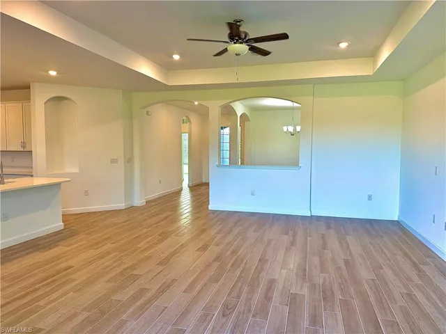 Unfurnished living room with a raised ceiling, recessed lighting, light wood-style flooring, a ceiling fan, and arched walkways
