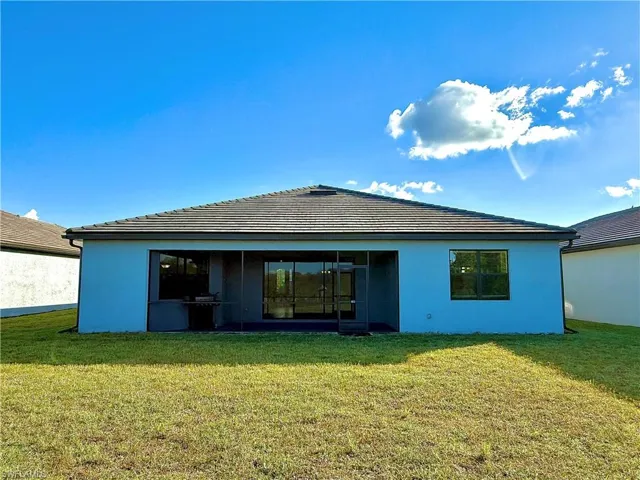 Rear view of house with a yard, stucco siding, and a tile roof