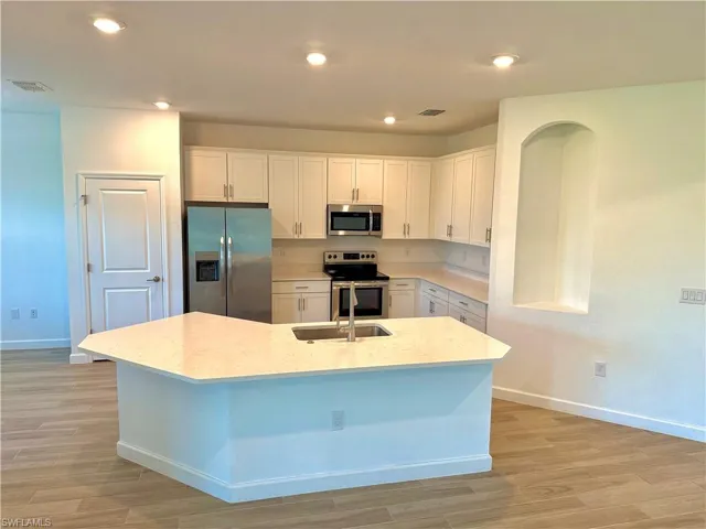Kitchen with white cabinetry, stainless steel appliances, recessed lighting, light stone counters, and light wood finished floors