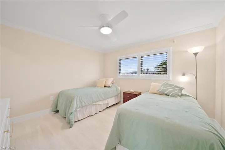 Bedroom with light wood-style floors, ornamental molding, and a ceiling fan