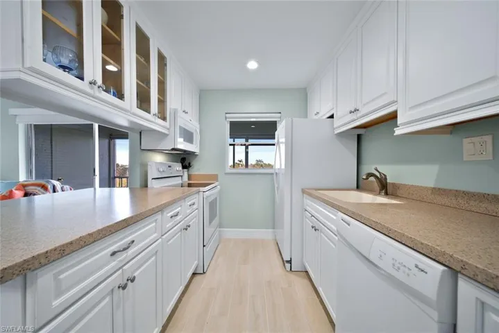 Kitchen featuring white cabinetry, glass insert cabinets, white appliances, light stone counters, and recessed lighting