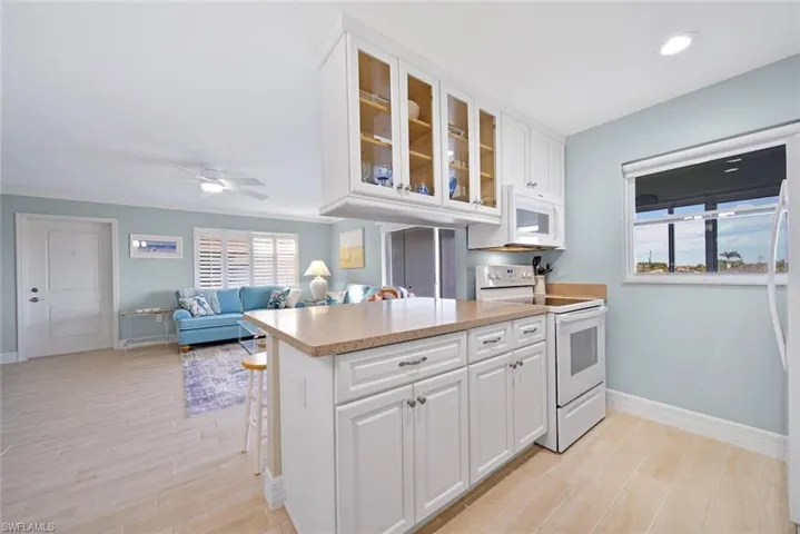 Kitchen featuring white cabinetry, white appliances, open floor plan, a peninsula, and glass insert cabinets
