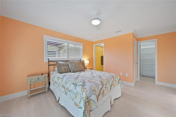 Bedroom with ornamental molding, light wood finished floors, a walk in closet, and a ceiling fan