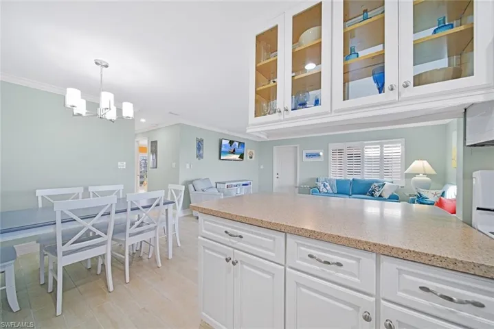 Kitchen featuring open floor plan, white cabinets, crown molding, light stone countertops, and decorative light fixtures