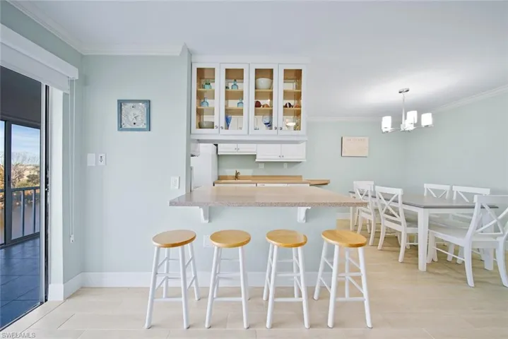 Bar with ornamental molding, glass insert cabinets, white cabinetry, freestanding refrigerator, and pendant lighting
