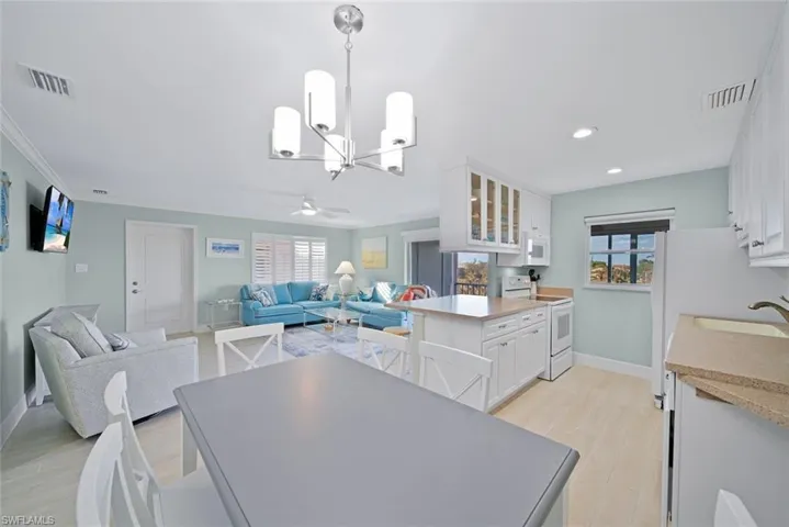 Kitchen featuring white cabinets, glass insert cabinets, white appliances, open floor plan, and hanging light fixtures