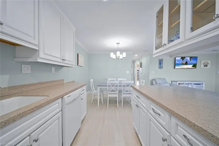 Kitchen featuring white cabinets, crown molding, dishwasher, decorative light fixtures, and a chandelier