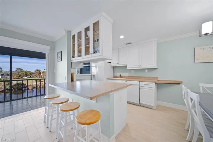 Kitchen featuring glass insert cabinets, white cabinets, crown molding, a breakfast bar, and white appliances