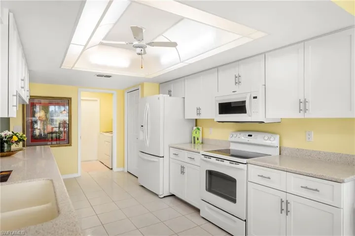 Kitchen with white appliances, a ceiling fan, white cabinetry, light tile patterned flooring, and light stone counters