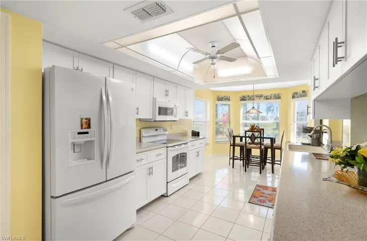 Kitchen with white appliances, ceiling fan, white cabinetry, light tile patterned floors, and a tray ceiling