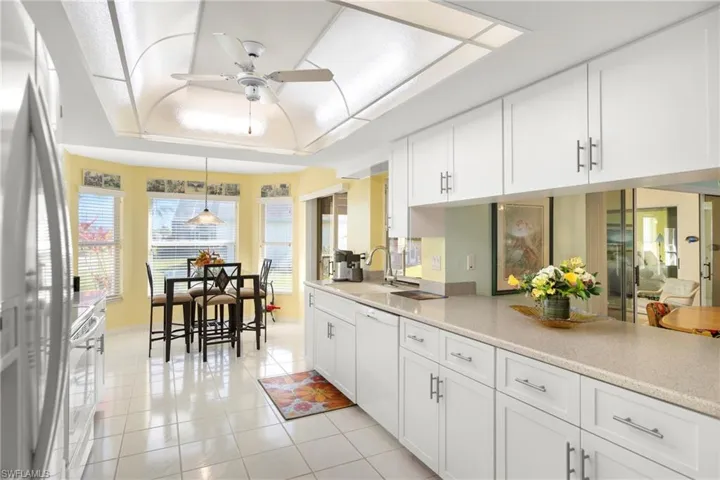 Kitchen with white cabinetry, white appliances, light countertops, light tile patterned floors, and a raised ceiling