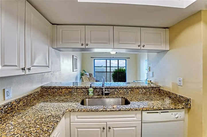 Kitchen with dishwasher, white cabinetry, dark stone countertops, a textured wall, and a peninsula