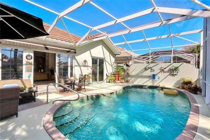 Screened-in pool deck featuring a curvilinear swimming pool with integrated steps, concrete paver patio, stucco exterior walls, and terracotta roof tiles