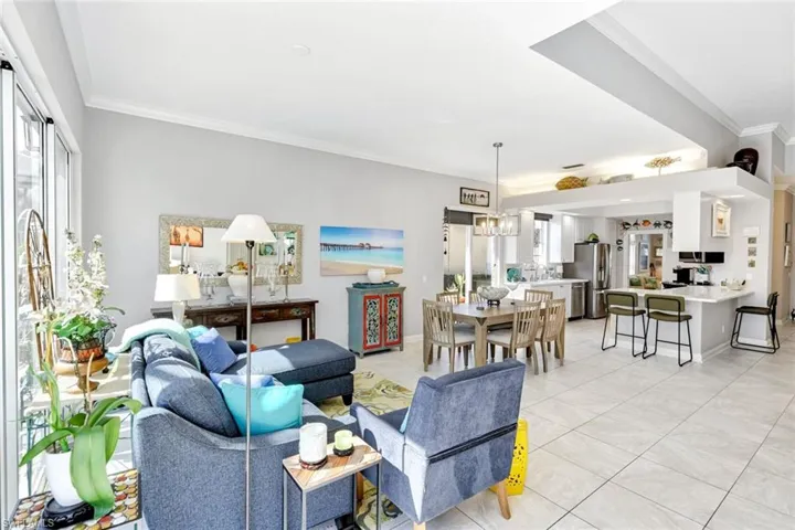 Bright, open-concept living space featuring light-toned tile flooring, high ceilings, and crown molding