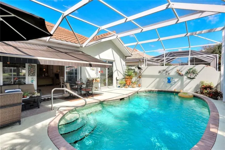 Screened-in pool deck featuring a freeform pool with steps, a paved surround, and an integrated retractable awning