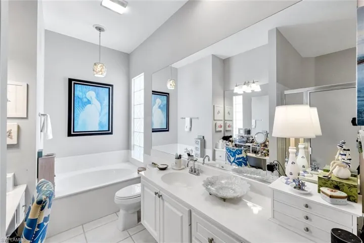 Bathroom featuring a built-in tub, dual sink vanity with white cabinetry, glass block window, and tile flooring